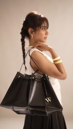 Woman holding a black handbag with a visible brand logo against a neutral background